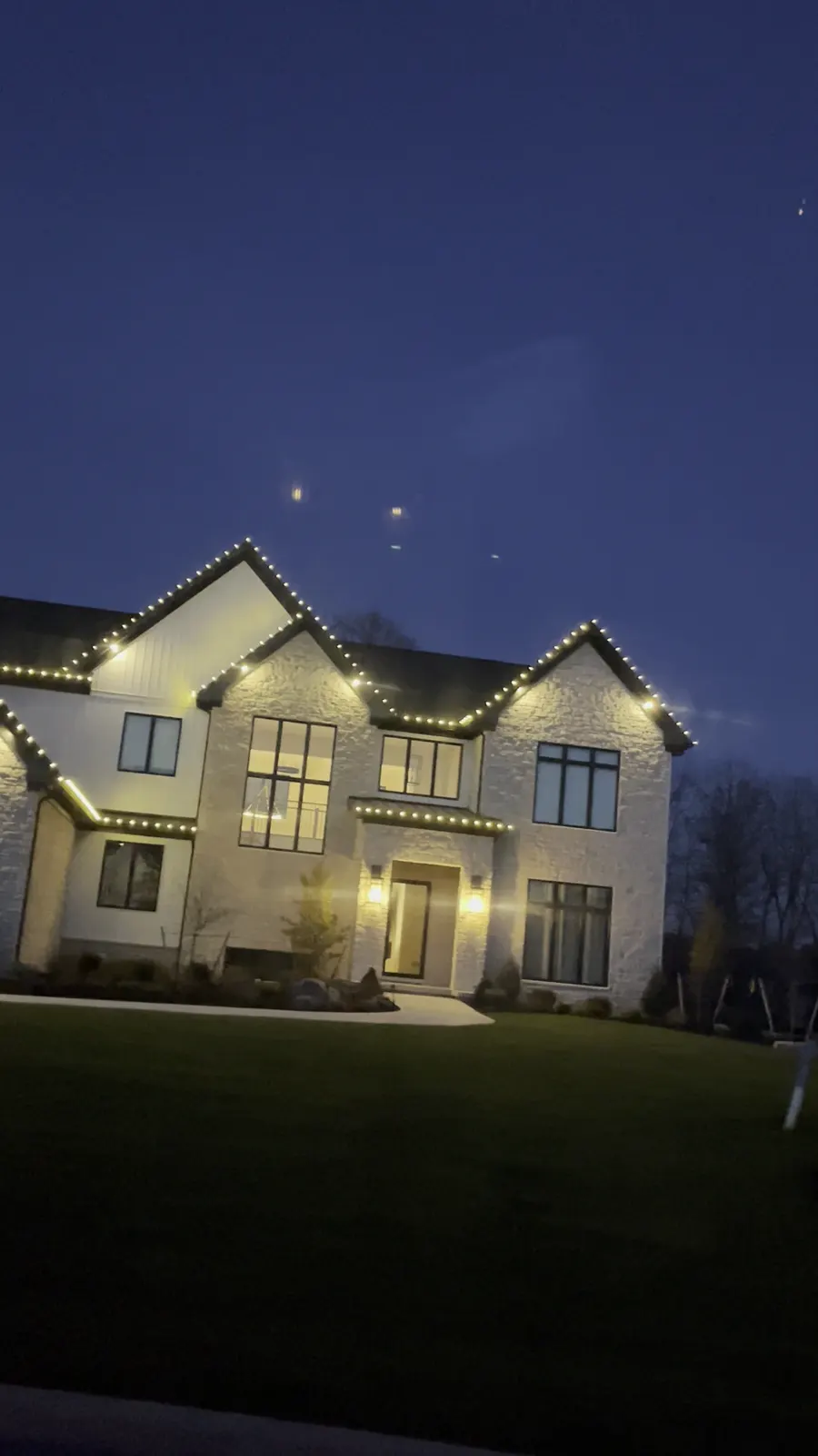 Modern farmhouse at blue hour with warm white bulbs on every gable