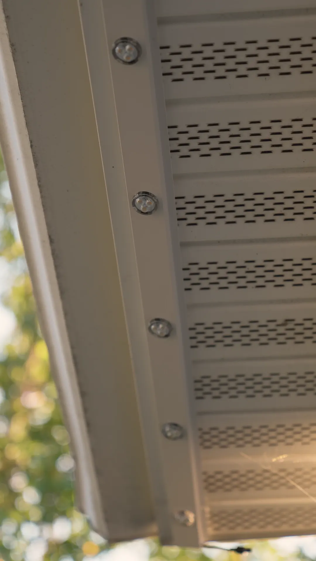 Close-up of the trim-colored aluminum channel with small puck lights set into it under a soffit, in daylight