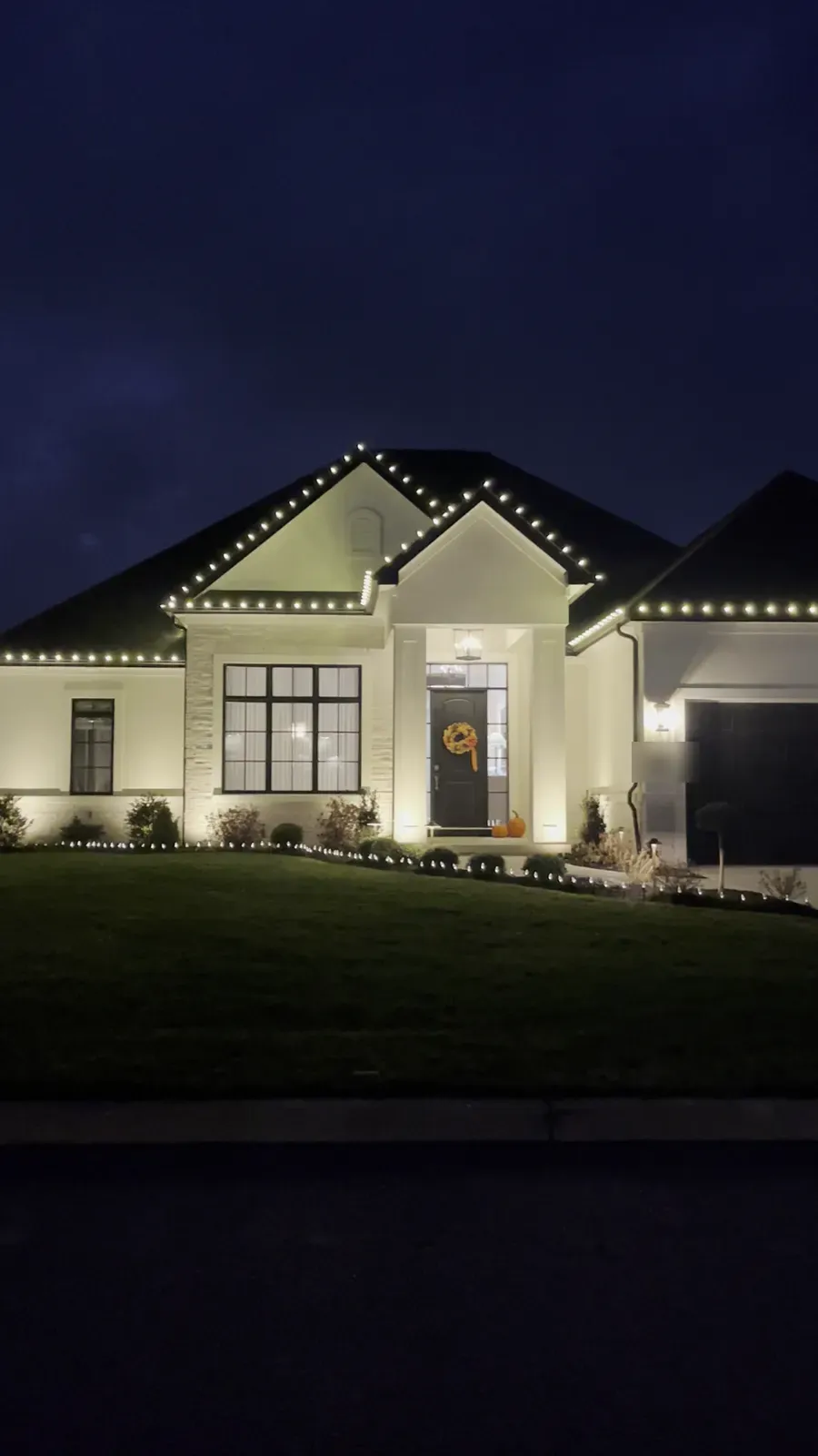 Ranch home in Clarence Center at dusk with white bulbs along the rooflines and garden bed